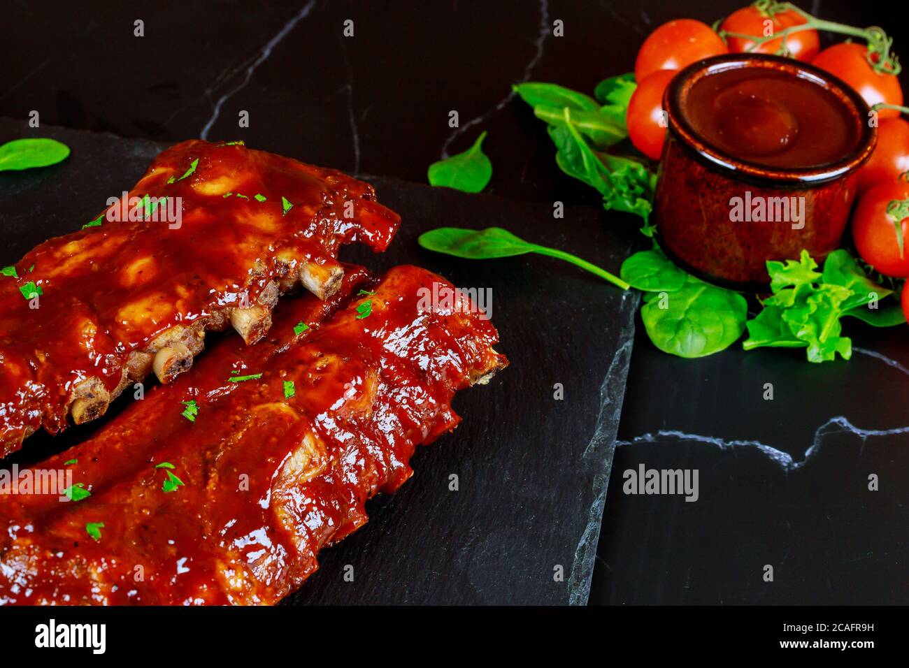 Côtes de porc avec sauce barbecue, tomates et épinards sur panneau en pierre noire. Vue de dessus. Banque D'Images
