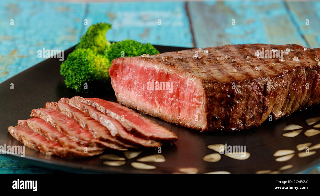 Tranche de rôti de bœuf rare sirloin avec brocoli sur une assiette noire. Banque D'Images