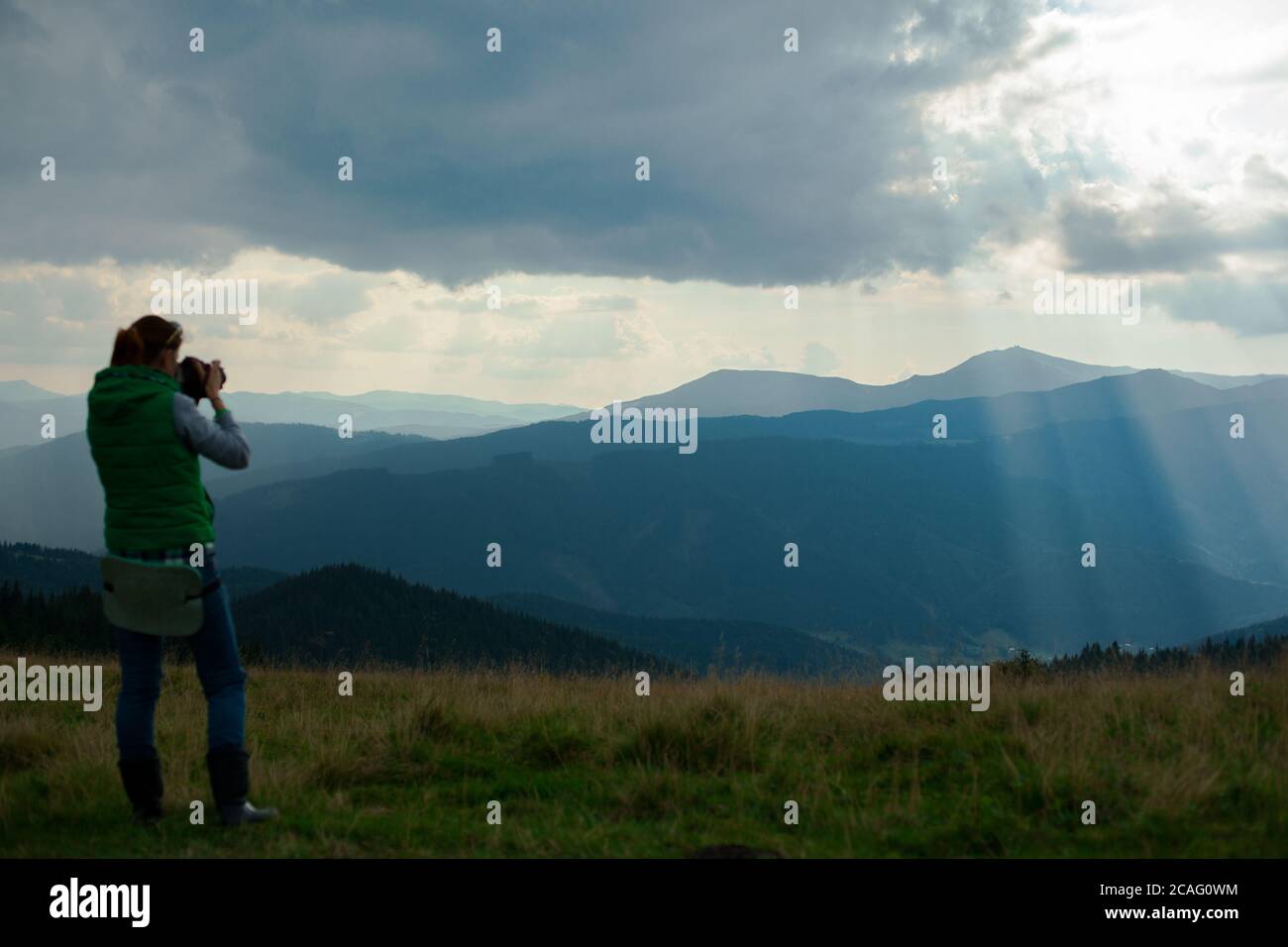 la photographe de fille dans les montagnes photographie le paysage sur le arrière-plan des rayons du soleil par jour nuageux Banque D'Images