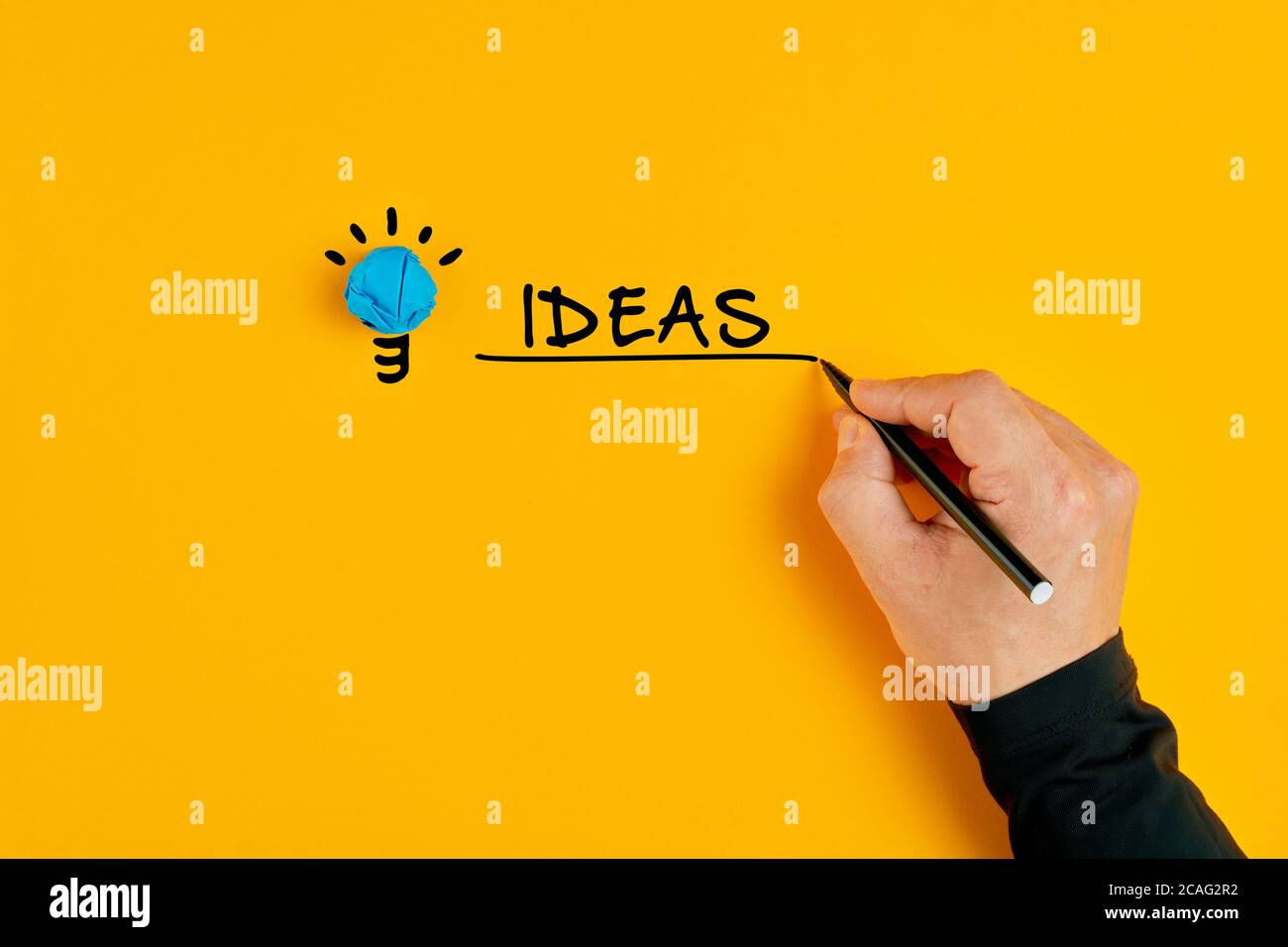 Main masculine écrivant le mot idées à côté d'une ampoule sur fond jaune. Concept d'idées créatives et d'innovation. Banque D'Images