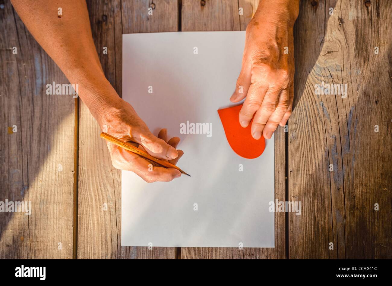 Femme âgée main allant écrire une lettre, coeur rouge sur table rustique en bois comme un fond, rayons du soleil. Vue de dessus, espace de copie. Mère ou femme, Banque D'Images