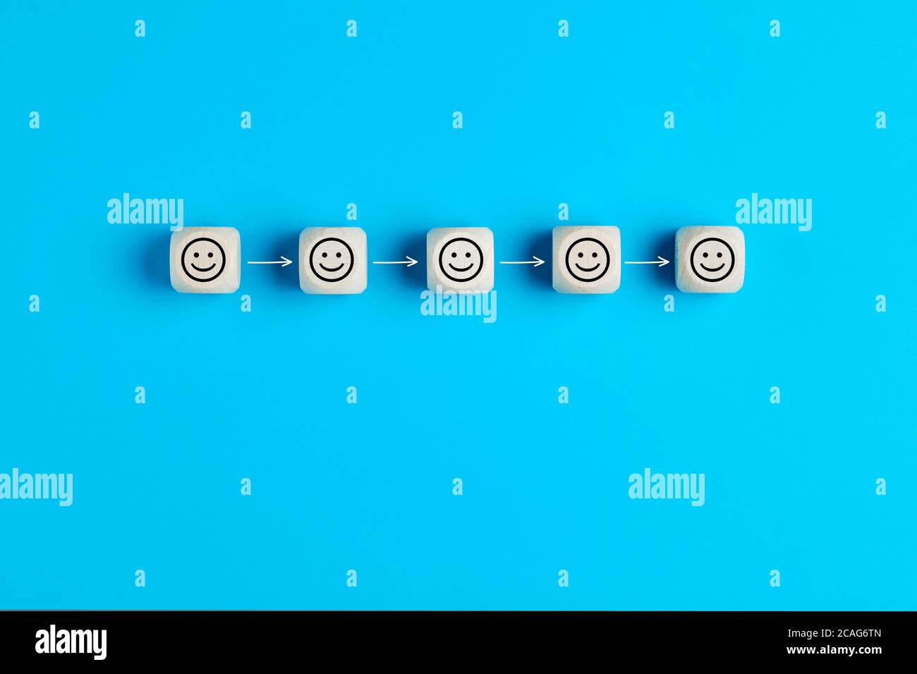 Concept de distanciation sociale. Blocs en bois avec des icônes de visage smiley éloignés par des flèches sur fond bleu. Banque D'Images