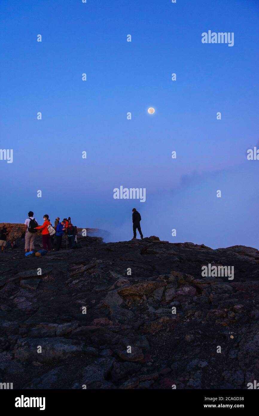 Silhouettes de personnes assises au bord du cratère du volcan Erta Ale, en Éthiopie, en pleine lune Banque D'Images