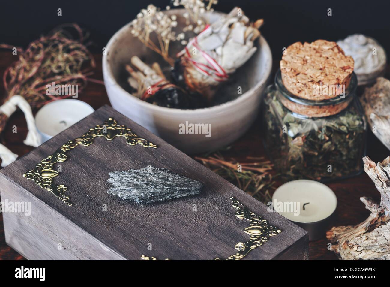 Roche en cristal de kyanite noire placée sur une boîte de sorcière en bois brun foncé. Gros plan avec diverses herbes séchées, plantes, fleurs, sauge bâton, bougies Banque D'Images