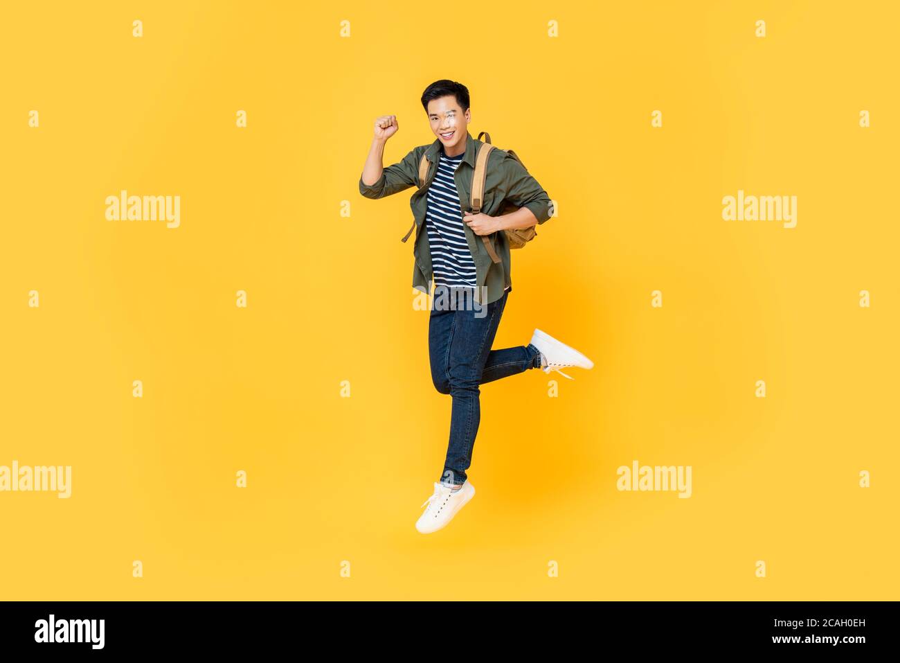 Joyeux souriant jeune touriste asiatique avec sac à dos sautant à l'intérieur milieu de l'air isolé sur fond jaune Banque D'Images