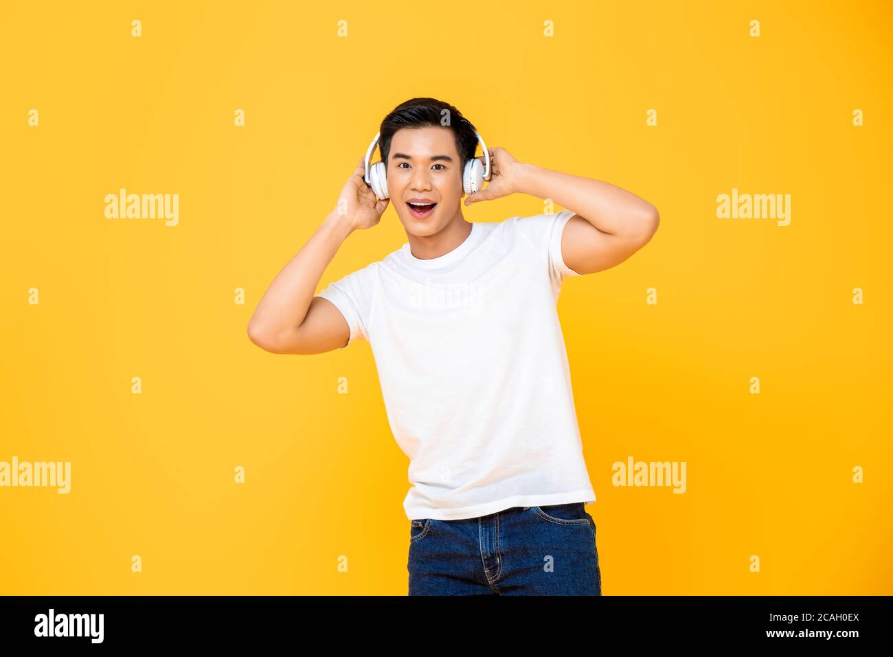Jeune homme asiatique élégant portant un casque pour écouter de la musique arrière-plan jaune Banque D'Images