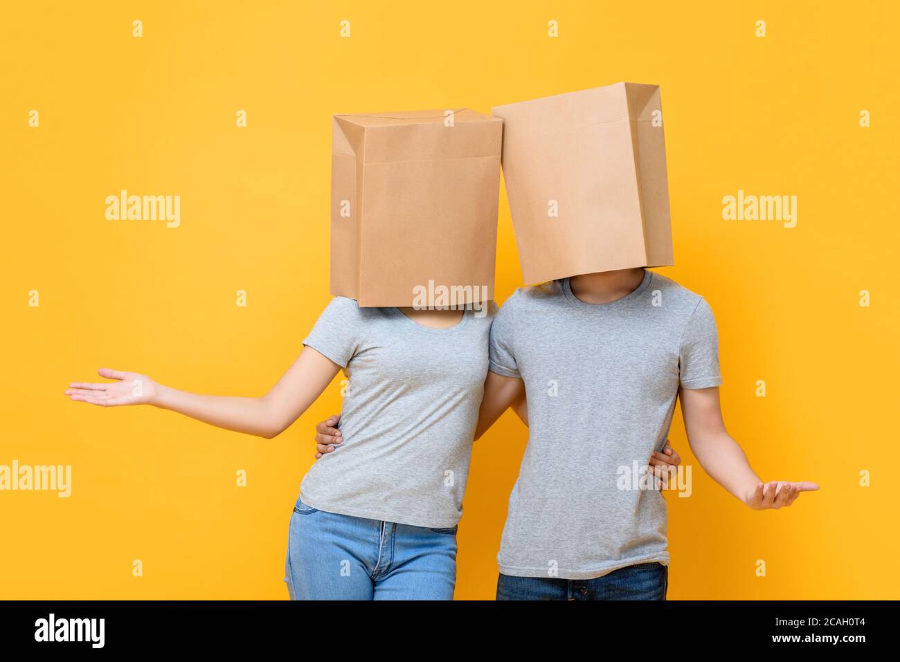 Couple anonyme sans visage couvrant les têtes avec des sacs en papier et la tenue chacun faisant un geste de main ouverte isolé sur jaune studio arrière-plan Banque D'Images