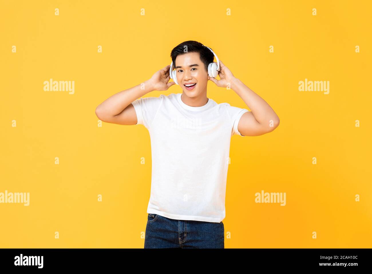 Joyeux jeune homme asiatique beau à écouter de la musique en streaming casque sans fil isolé sur fond jaune studio Banque D'Images