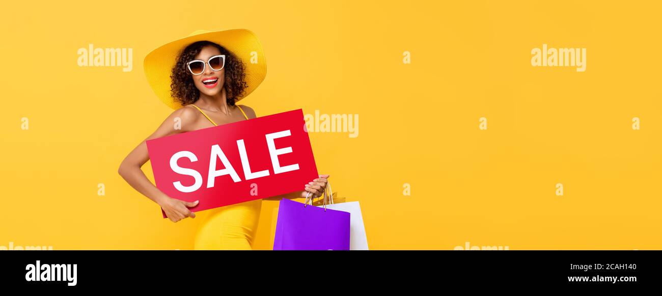 Femme afro-américaine portant une affiche rouge avec des sacs à provisions isolé sur fond de bannière jaune studio avec espace de copie Banque D'Images