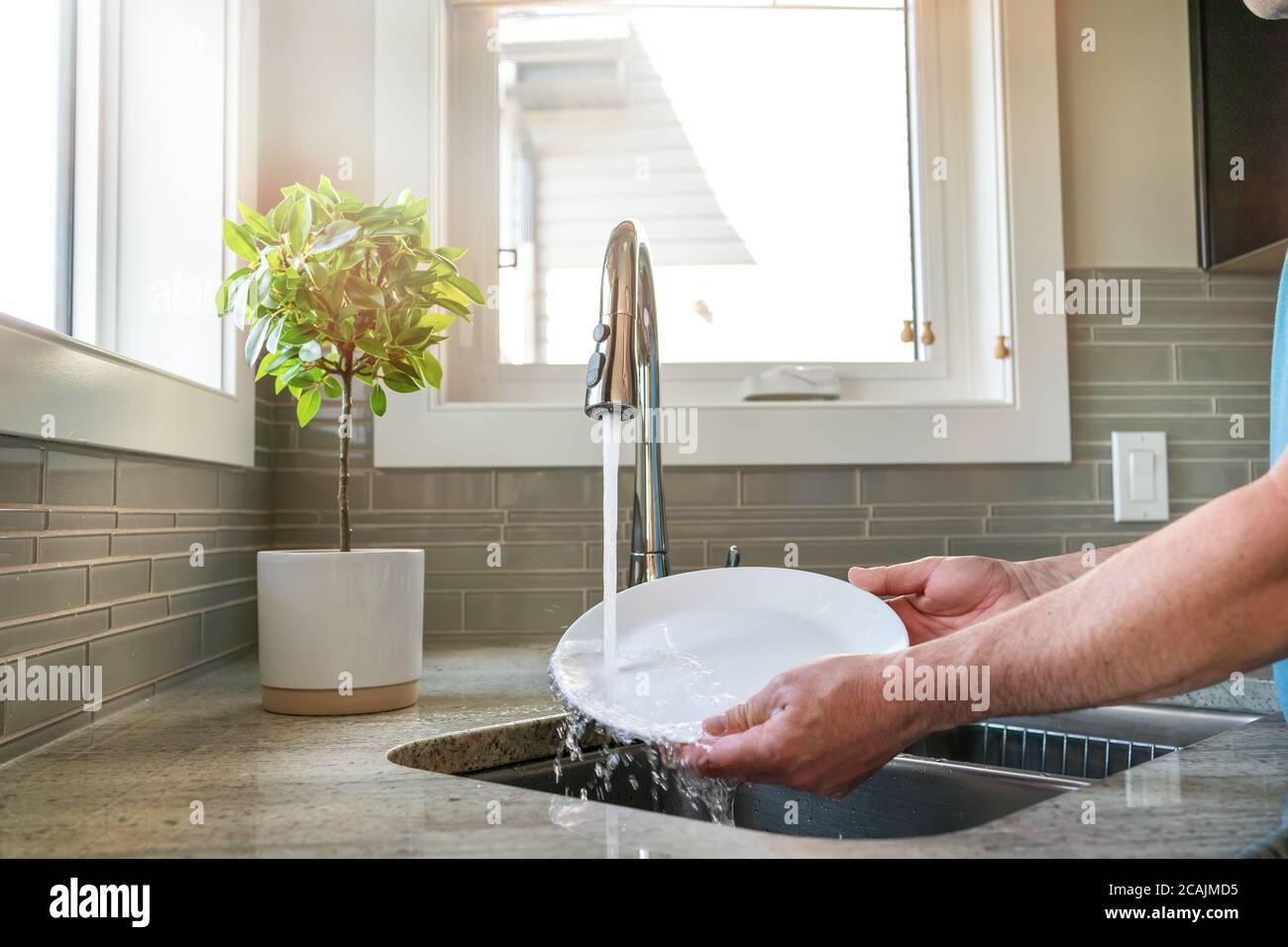 Un homme qui fait des plats, se laver dans un évier de cuisine, vue rapprochée. Nettoyage des minerais. Lave-vaisselle : lave une plaque blanche dans un évier. Banque D'Images