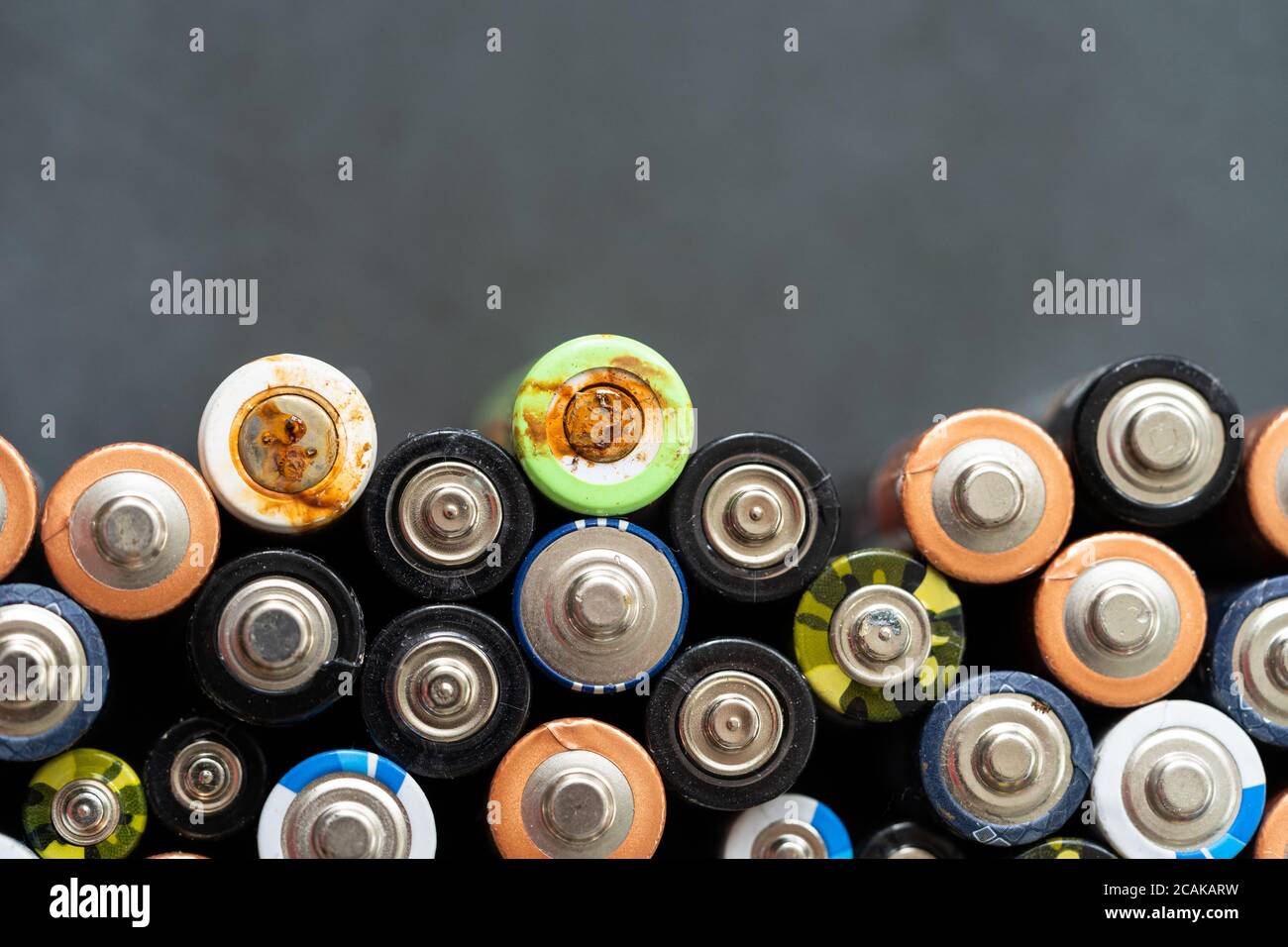 Gros plan des extrémités positives des batteries déchargées de différentes tailles et formats sur fond noir, mise au point sélective. Pile alcaline usagée avec corr Banque D'Images