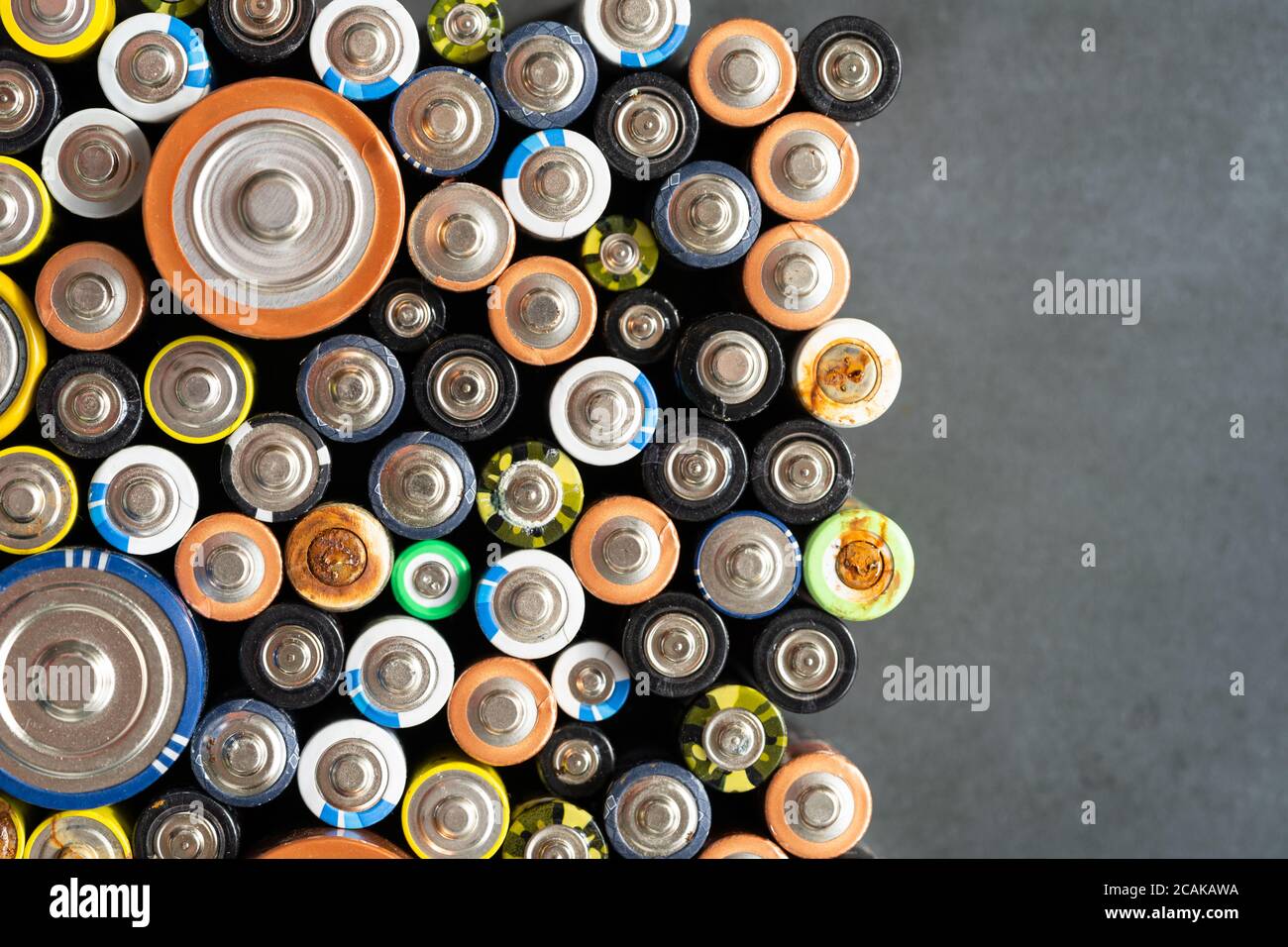 Gros plan des extrémités positives des batteries déchargées de différentes tailles et formats sur fond noir, mise au point sélective. Pile alcaline usagée avec corr Banque D'Images