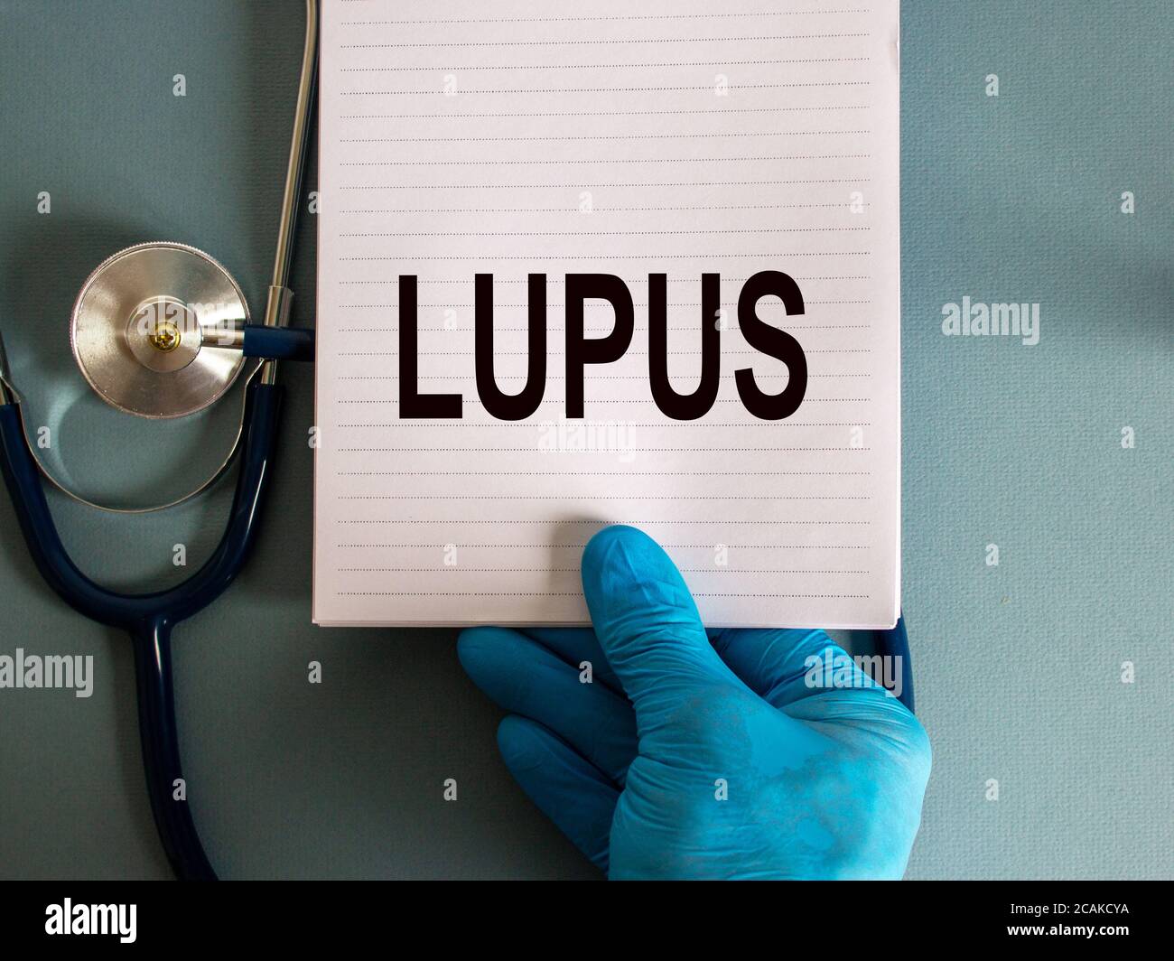 Main dans un gant bleu, carte blanche avec mot lupus et stéthoscope. Banque D'Images