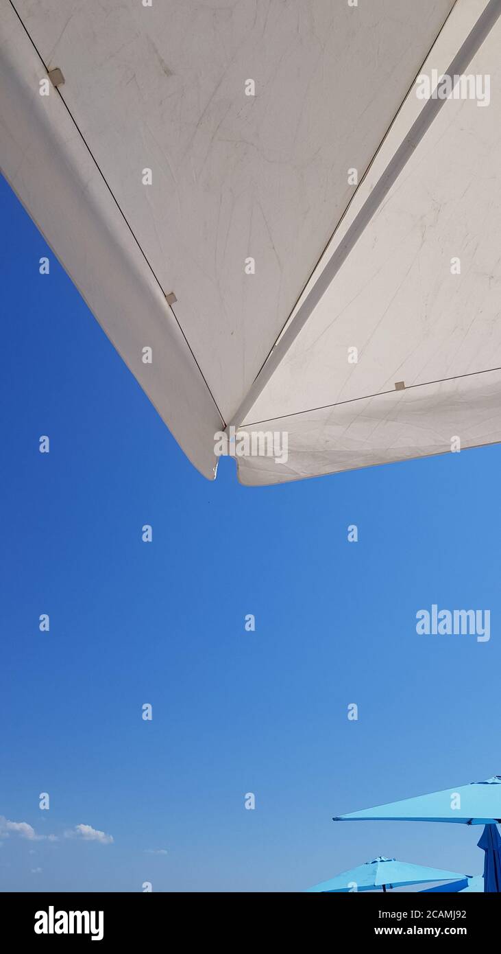 Arrière-plan d'été minimal avec des formes géométriques de parasols de plage avec un ciel bleu dégradé. Géométrie des pare-soleil blancs et bleus Banque D'Images