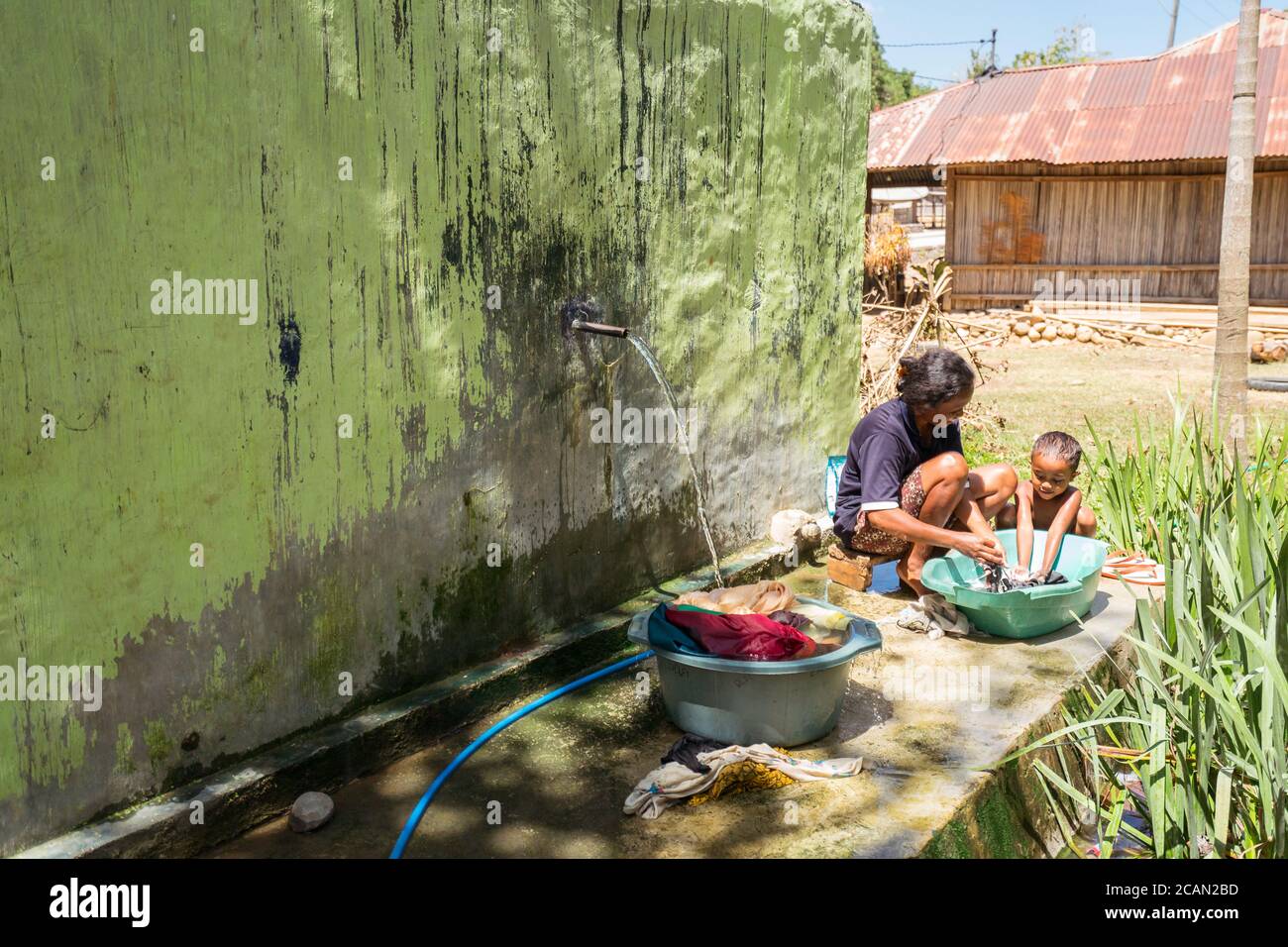 Haikesa / Indonésie - 10 août 2018 : la mère et la petite fille se lavent les vêtements à la main près de la fontaine du village Banque D'Images