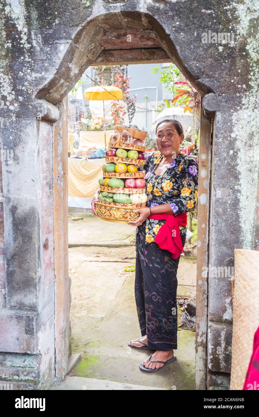 Bali / Indonésie - 15 août 2018 : Portrait d'une femme bouddhiste souriant à la porte d'un petit temple local tenant des fruits comme offrande religieuse Banque D'Images