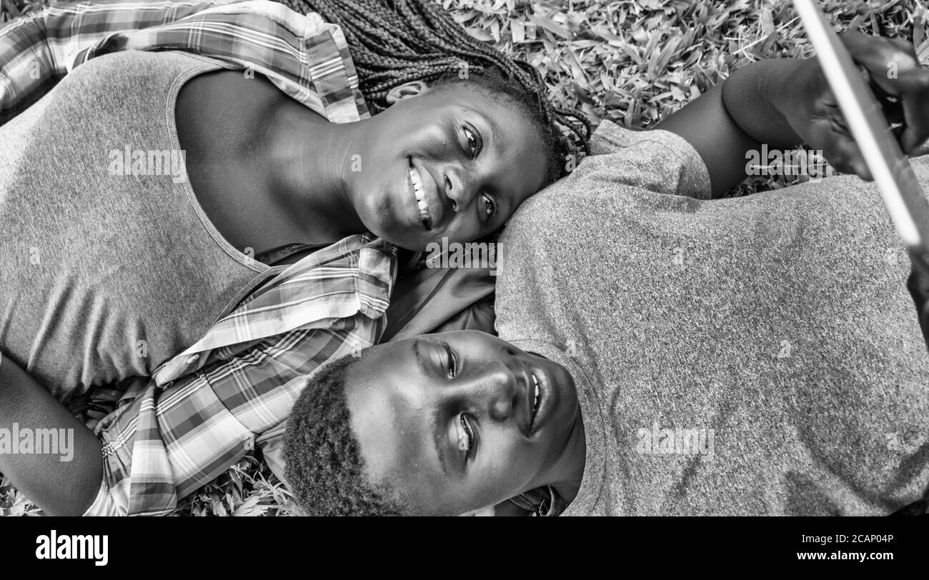 Deux adolescents africains se reposant sur l'herbe à l'aide d'une tablette. Bak au concept d'école Banque D'Images