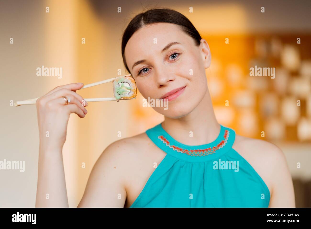 Portrait d'une belle femme mangeant un rouleau de sushi, nourriture japonaise saine. Belle femme tenant des baguettes avec des sushis près de son visage Banque D'Images