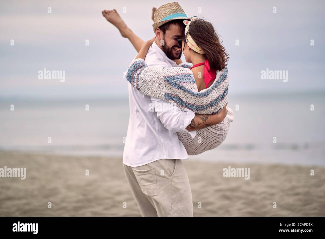un gars de barbe caucasien portant sa petite amie dans ses bras à la plage Banque D'Images