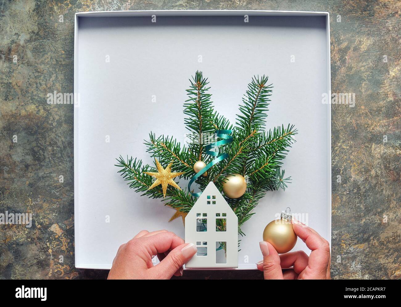 Décorations de Noël, plat avec les mains des femmes. Fabrication boîte décorée avec silhouette de maison, brindilles de sapin et breloques dorées, boules. Poser à plat sur dar Banque D'Images