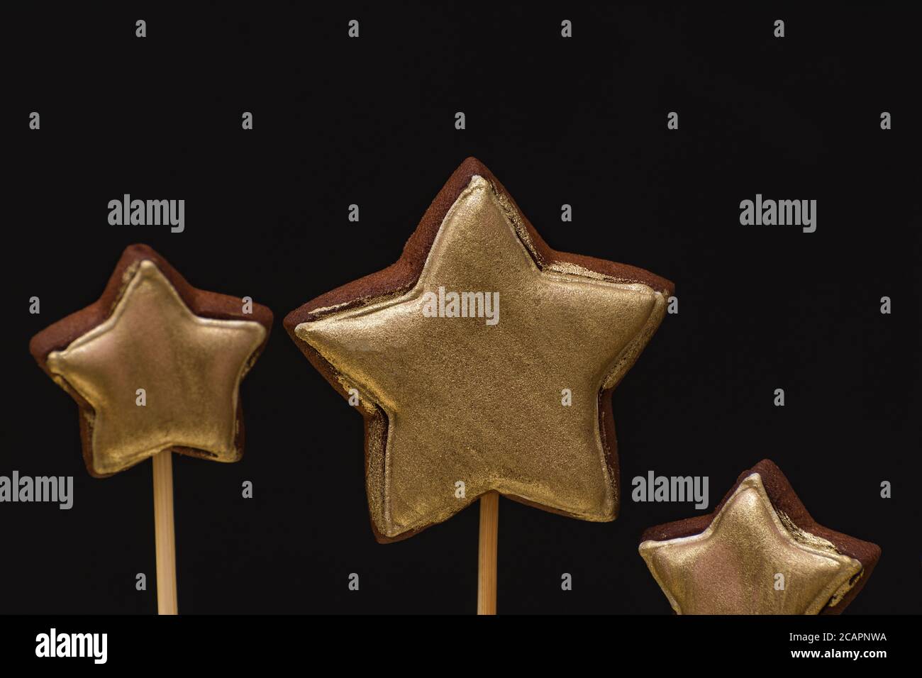 Biscuits de pain d'épice de couleur or sur un bâton sur fond noir. Banque D'Images