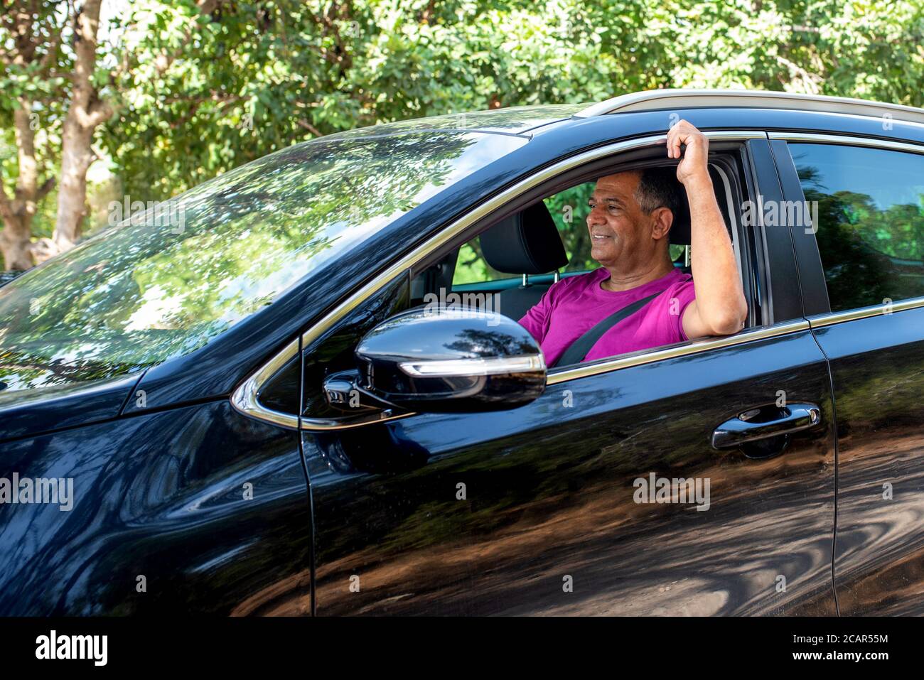 Vue de profil d'un homme âgé heureux au milieu des années 60 au volant d'une voiture. Homme conduisant une voiture en forêt. Banque D'Images