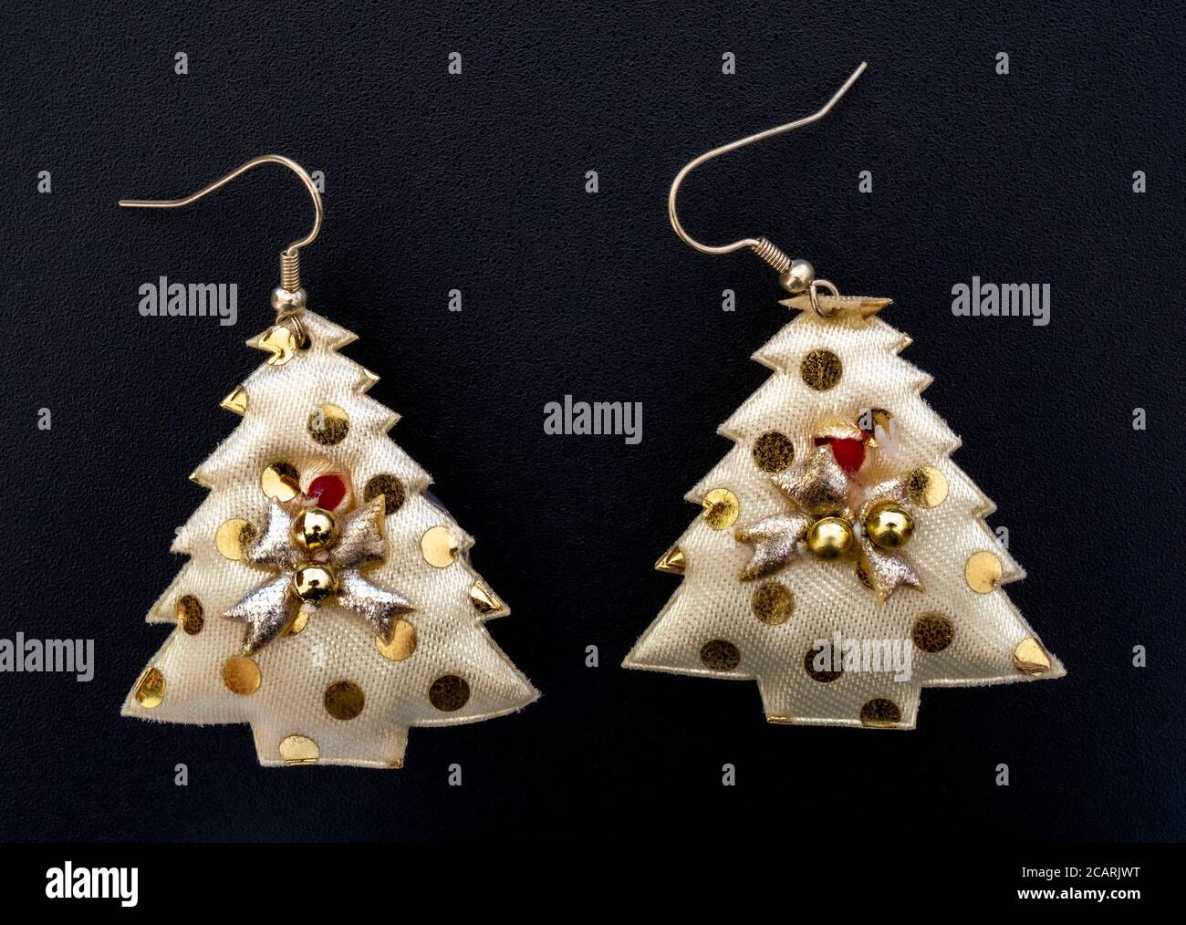 Gros plan de dessus de POV d'une paire de boucles d'oreilles en forme d'arbre de Noël – en tissu piqué et rembourré, avec des points et des boules de couleur or. Banque D'Images