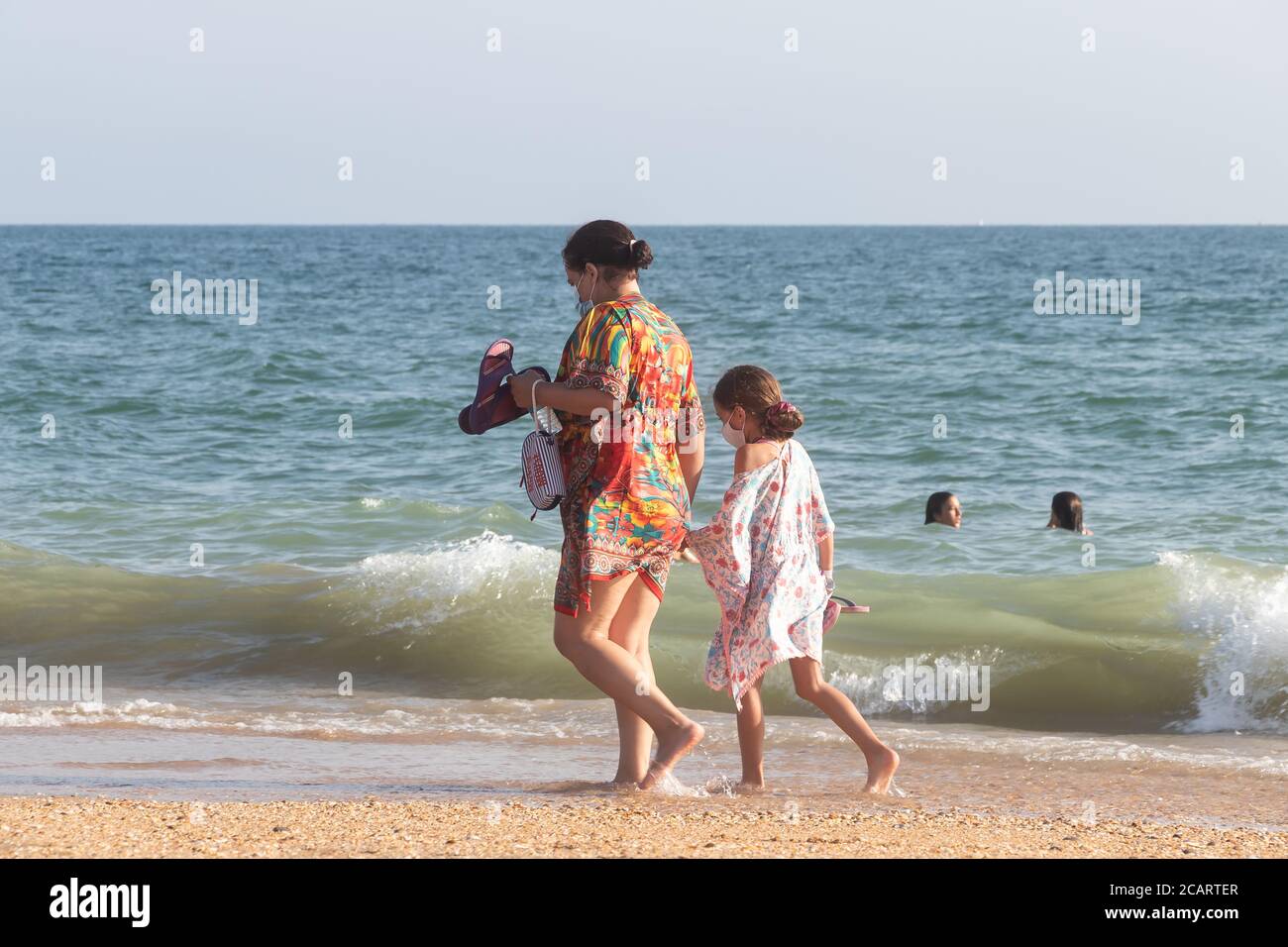 Punta Umbria, Huelva, Espagne - 7 août 2020: La mère et la fille marchent sur la plage en portant des masques protecteurs ou médicaux. Nouveau normal au spa Banque D'Images