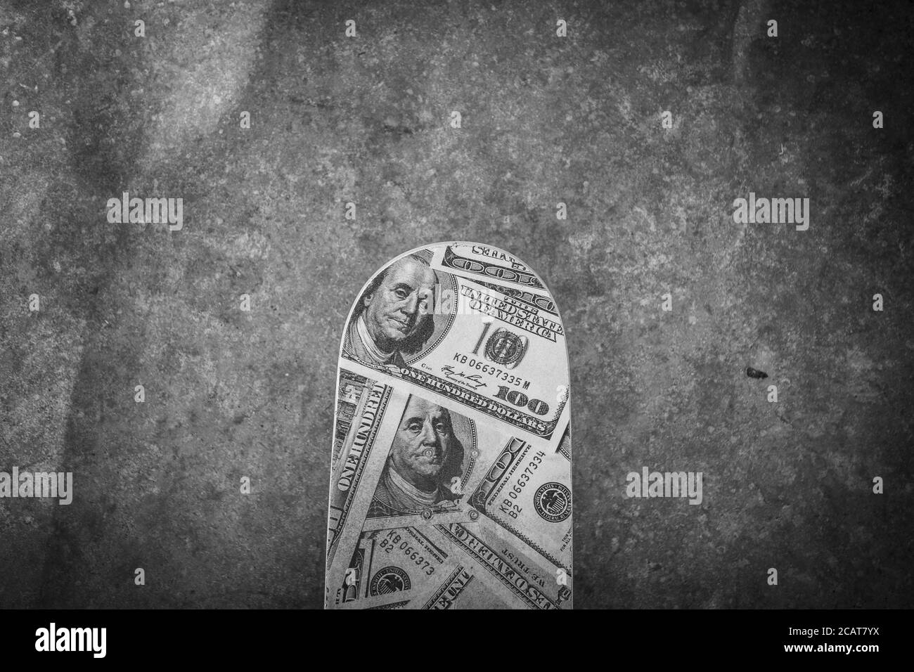 Photo en hauteur en niveaux de gris d'un skateboard avec des panneaux de dollar le sol Banque D'Images