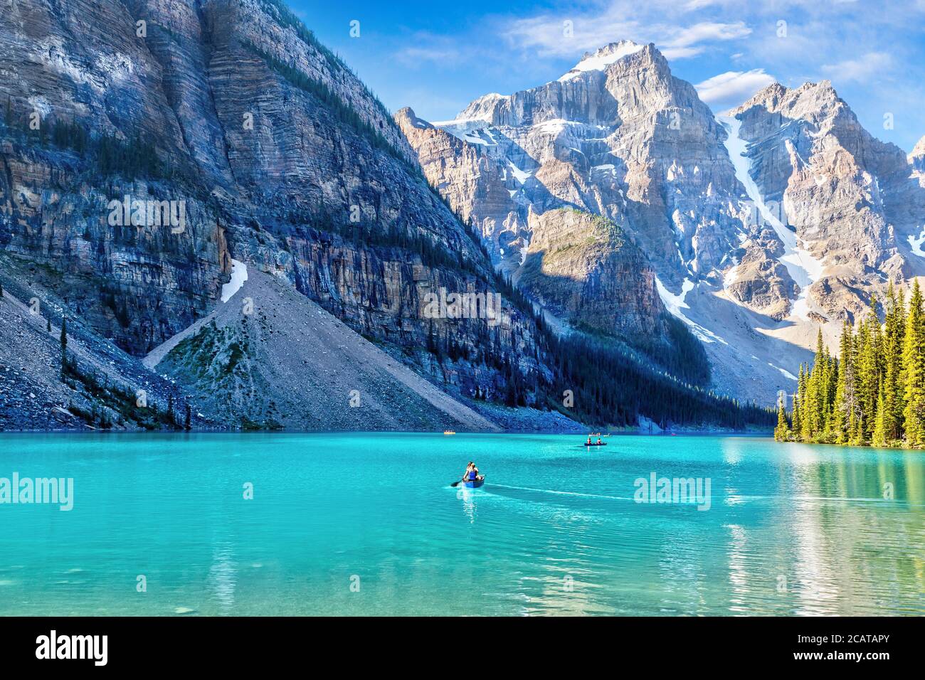Des visiteurs non identifiables font du canoë sur leurs bateaux sur le lac Moraine de couleur turquoise dans les Rocheuses canadiennes du parc national Banff, près du lac Louise. Le va Banque D'Images