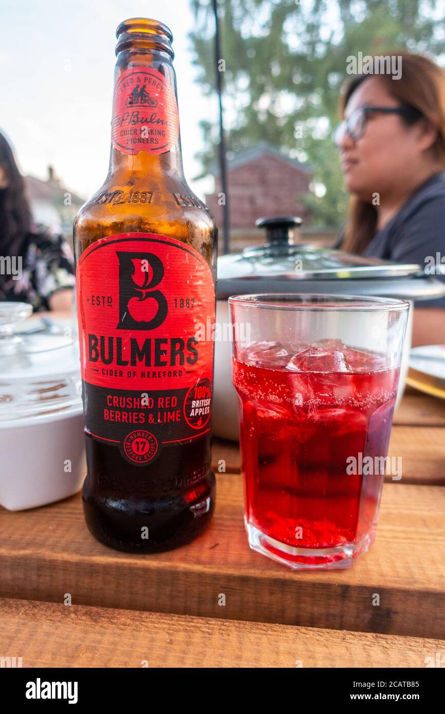Une bouteille de Bulmers saveur de baies rouges et de citron vert et un verre avec de la glace à l'extérieur sur une table en bois. Banque D'Images