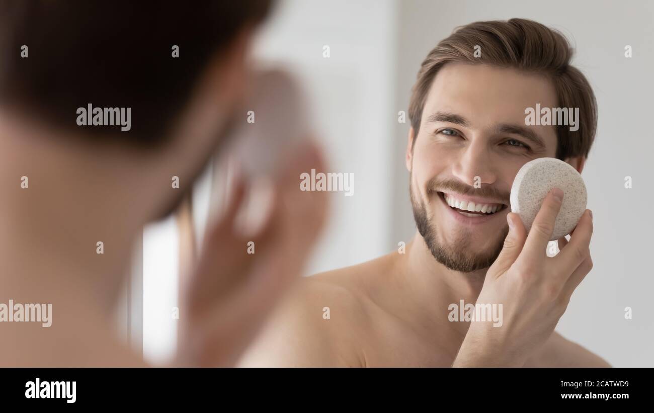 Gros plan miroir réflexion homme souriant à l'aide d'une éponge nettoyante pour le visage Banque D'Images