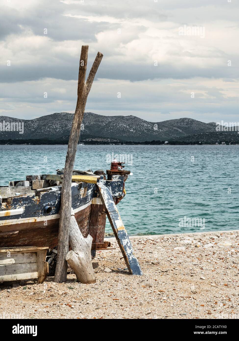 Vider le vieux bateau de pêche rouillé sur le rivage de la mer dans le calme nuageux journée. Collines en arrière-plan. Tir vertical. Banque D'Images