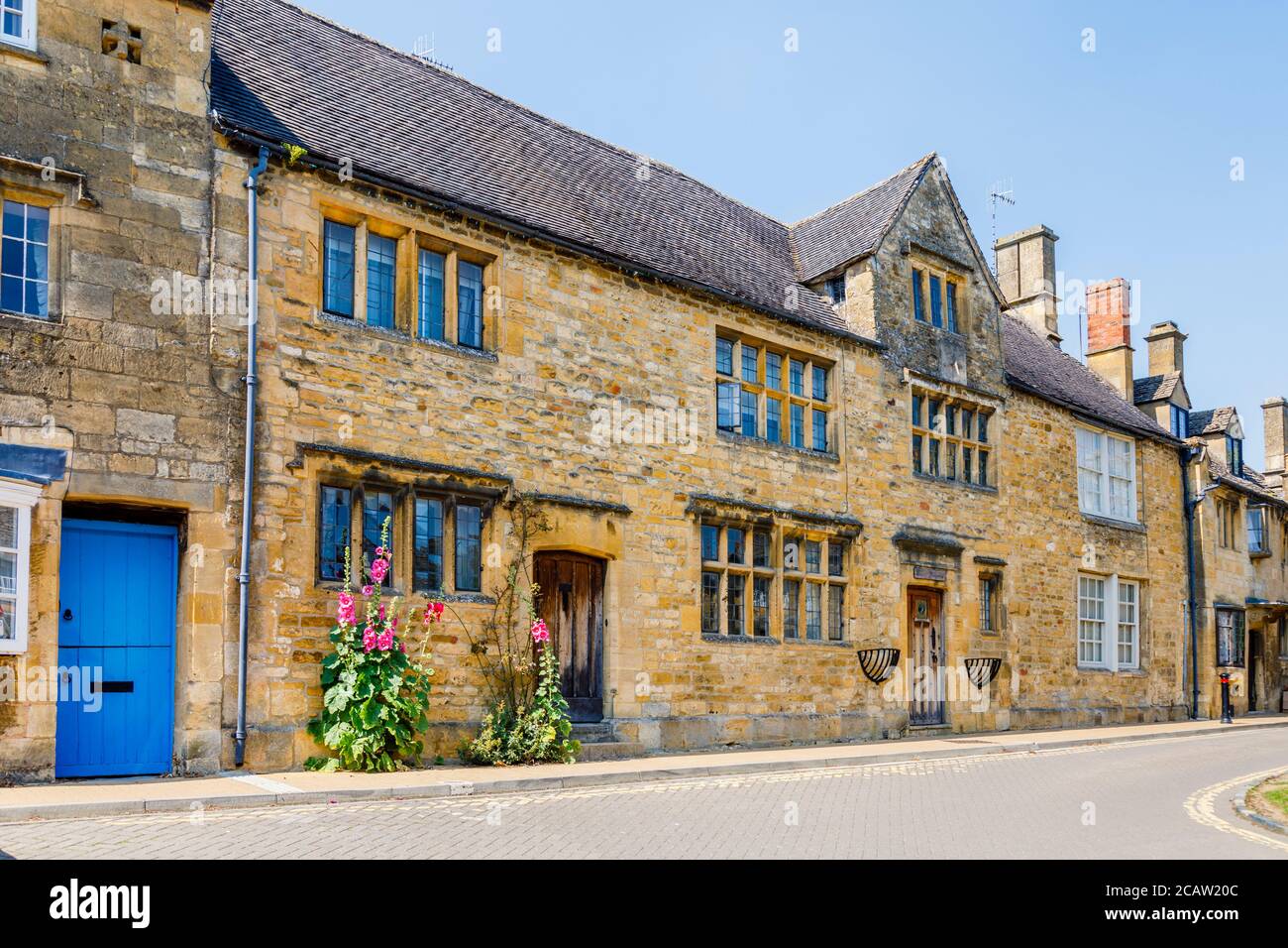 Vue rapprochée de trous de creux roses à rouges (Alcea rosea) poussant contre un mur à l'extérieur d'un cottage à Chipping Campden, une ville de marché dans les Cotswolds Banque D'Images