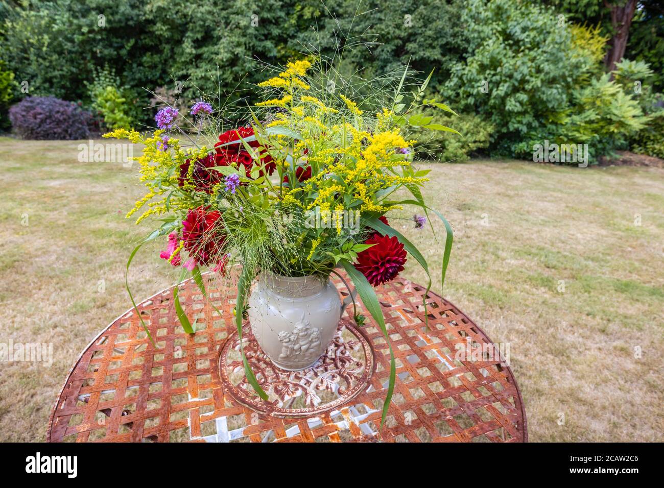 Arrangement de fleurs: Une exposition de fleurs d'été cueillies dans un jardin anglais mélangé disposés dans une cruche de drabware sur une table de jardin en métal d'époque rouillée Banque D'Images