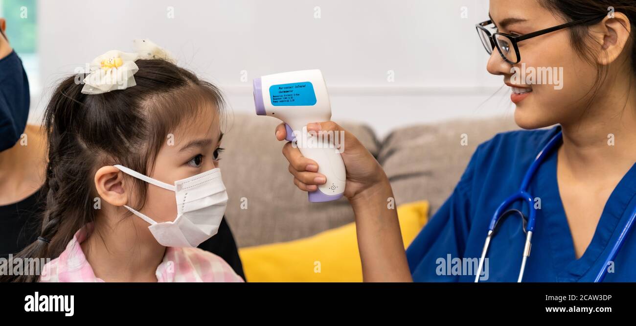 Panoramique asiatique femme médecin utilisez un thermomètre infrarouge pour prendre la température à la petite fille enfant dans le salon pendant que le médecin visite à la maison. Santé à domicile Banque D'Images