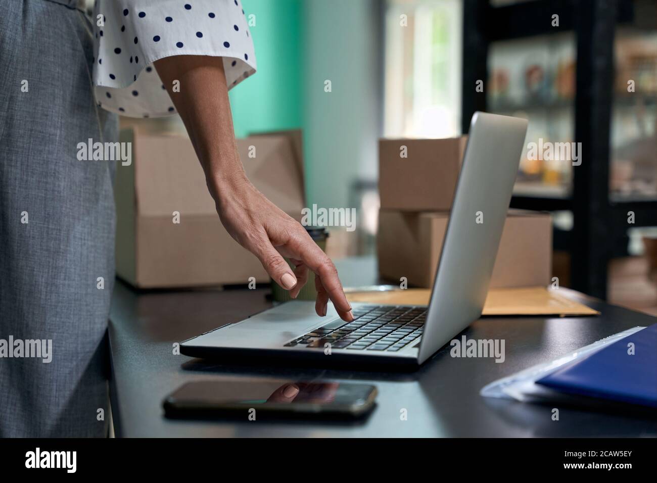 Prendre des commandes en ligne. Prise de vue rognée d'une femme, propriétaire d'entreprise, utilisant un ordinateur portable, debout dans son magasin ou dans son magasin. Concentrez-vous sur la main féminine. Petite entreprise, vente au détail Banque D'Images