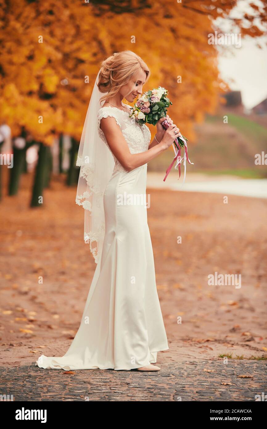 Belle mariée en robe longue blanche est odorant bouquet de mariage dans le  parc d'automne le jour du mariage Photo Stock - Alamy