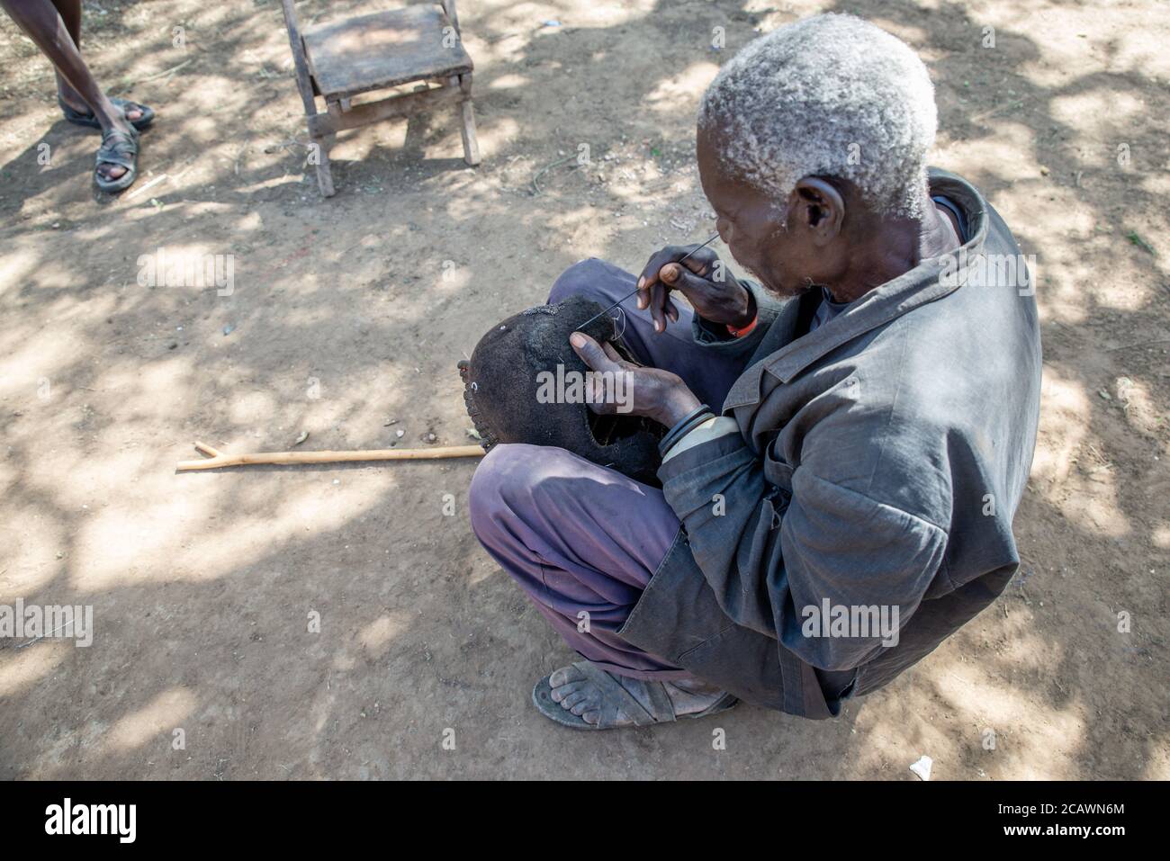 Ancien homme de Karamojong maintenant un étimat (epukot) hdeaddress fait de cheveux humains et de plumes d'autruche, district de Moroto, Ouganda Banque D'Images