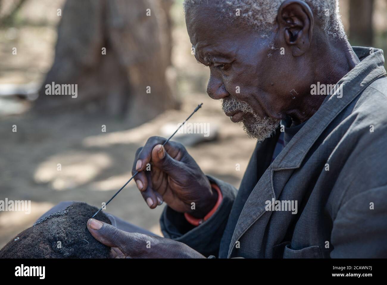 Ancien homme de Karamojong maintenant un étimat (epukot) hdeaddress fait de cheveux humains et de plumes d'autruche, district de Moroto, Ouganda Banque D'Images