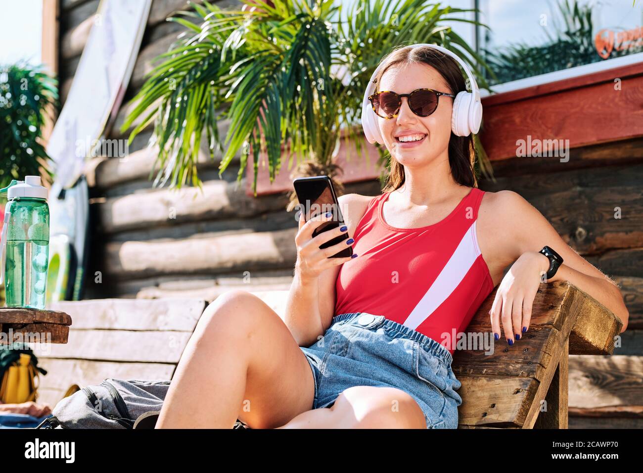 Jeune femme gaie dans un casque, des lunettes de soleil, une table de cuisson rouge et un short en denim Banque D'Images