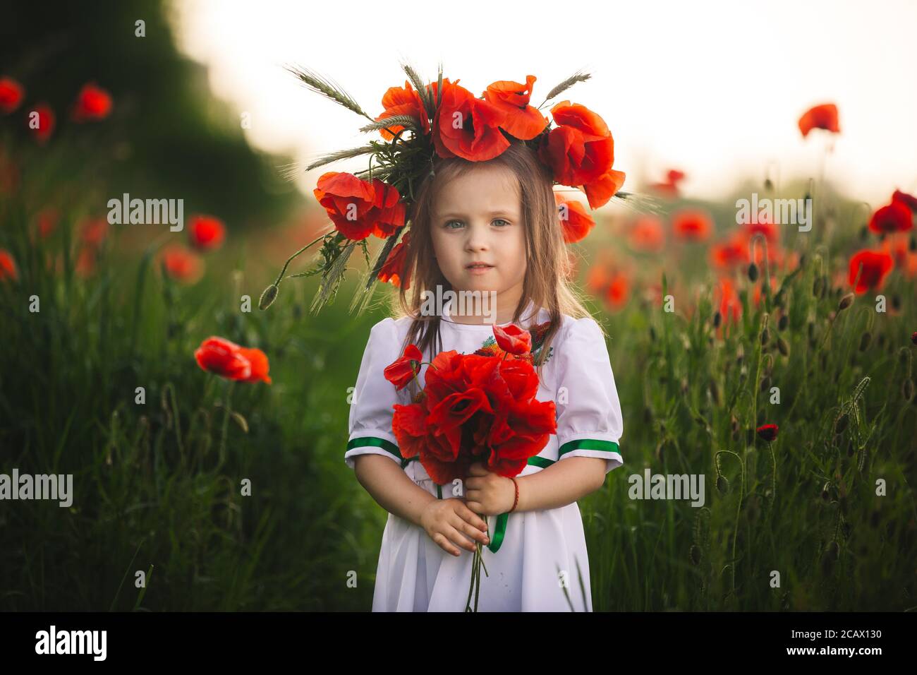 belle petite fille avec une couronne de coquelicots dans une robe blanche  et un bouquet de fleurs sauvages. enfant mignon dans champ de coquelicot  Photo Stock - Alamy