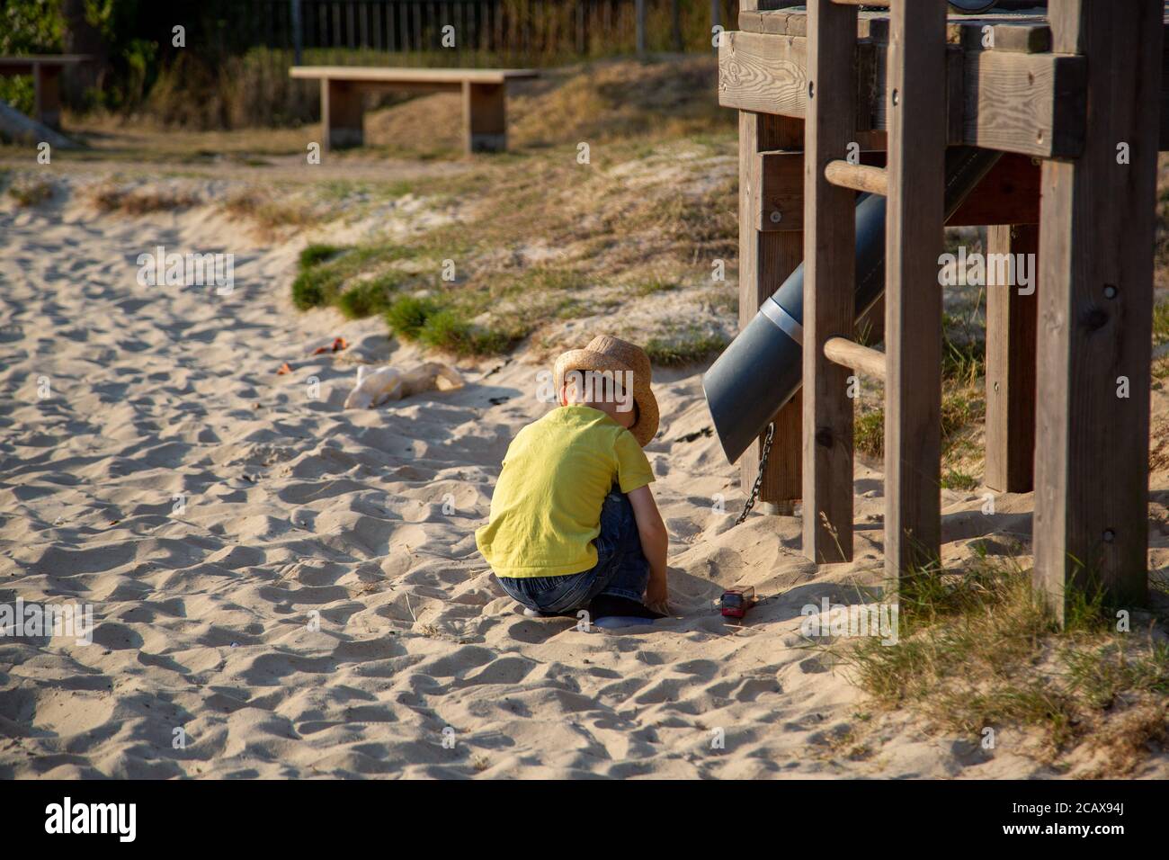 Un petit garçon jouant dans un bac à sable dans un parc pendant l'été avec un cadre d'escalade en vue Banque D'Images