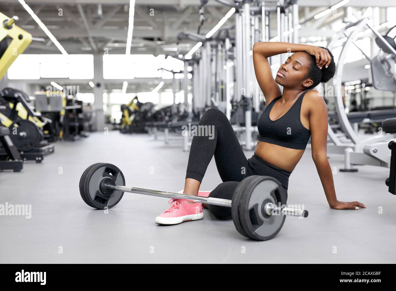 black afro fit femme fatiguée après des exercices haltérophilie, jeune femme assis à côté de barbell, épuisé Banque D'Images