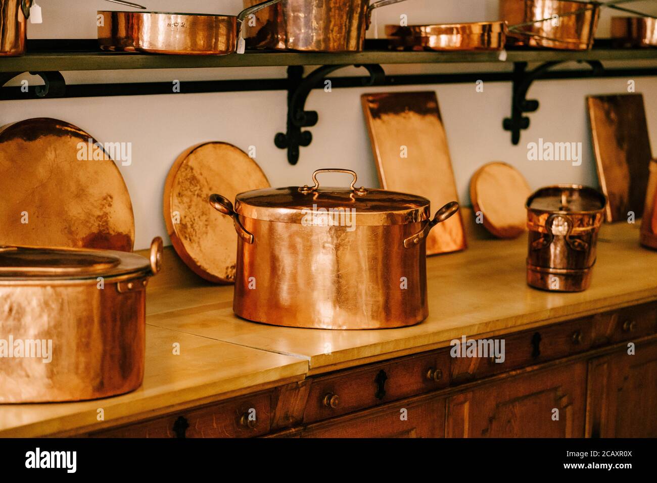 Grandes casseroles en cuivre avec dessous de verre chauds sur le comptoir avec casseroles en cuivre et casseroles sur les étagères à fixer au mur blanc. Banque D'Images