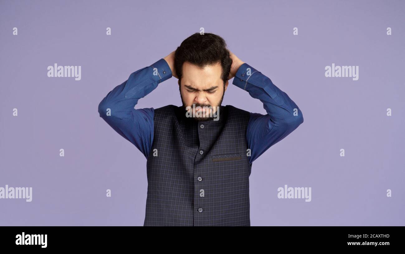 Émotions négatives. Un gars indien désespéré piller ses cheveux sur fond lilas Banque D'Images