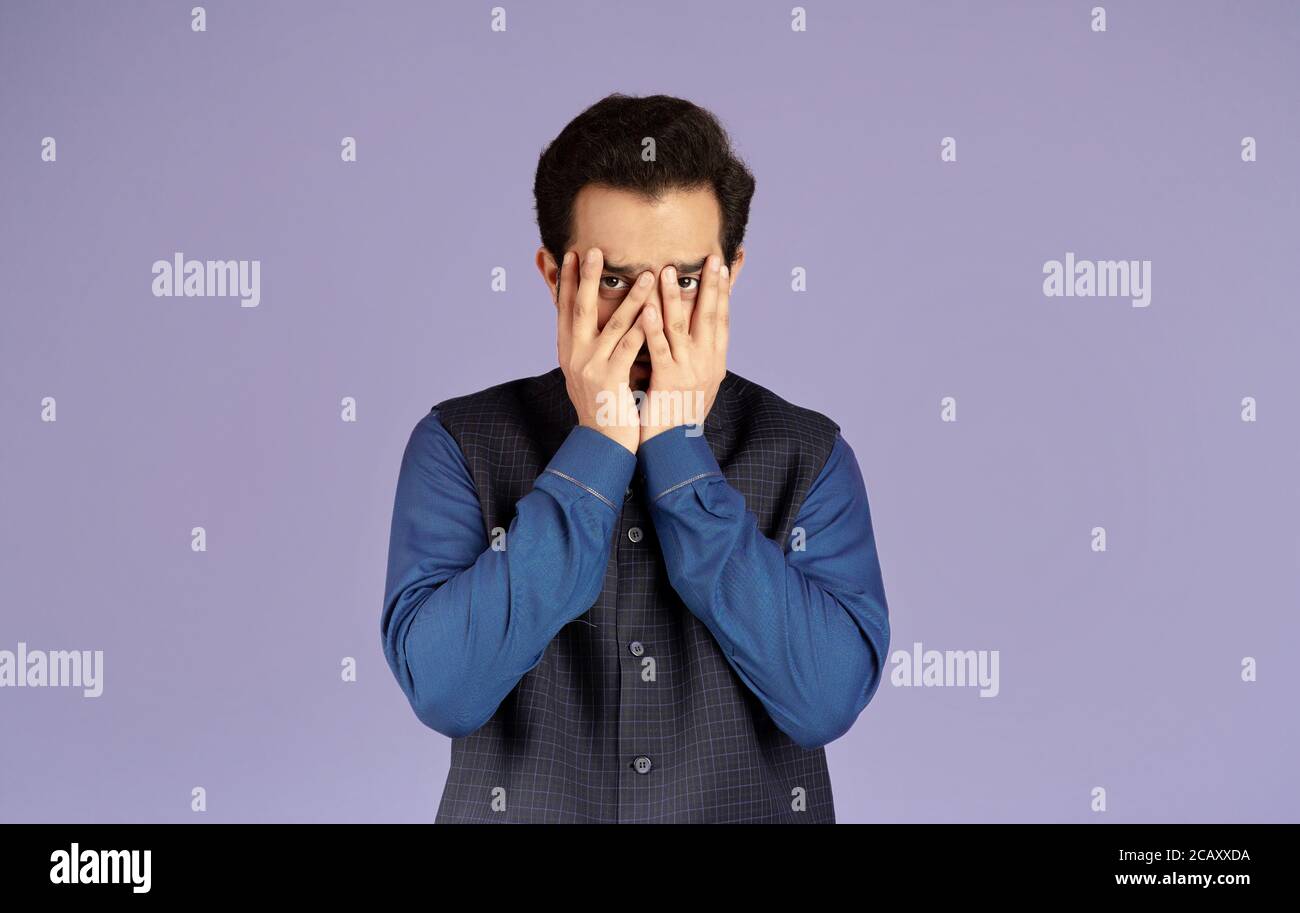 Homme indien émotif couvrant le visage avec ses mains sur le lilas arrière-plan Banque D'Images