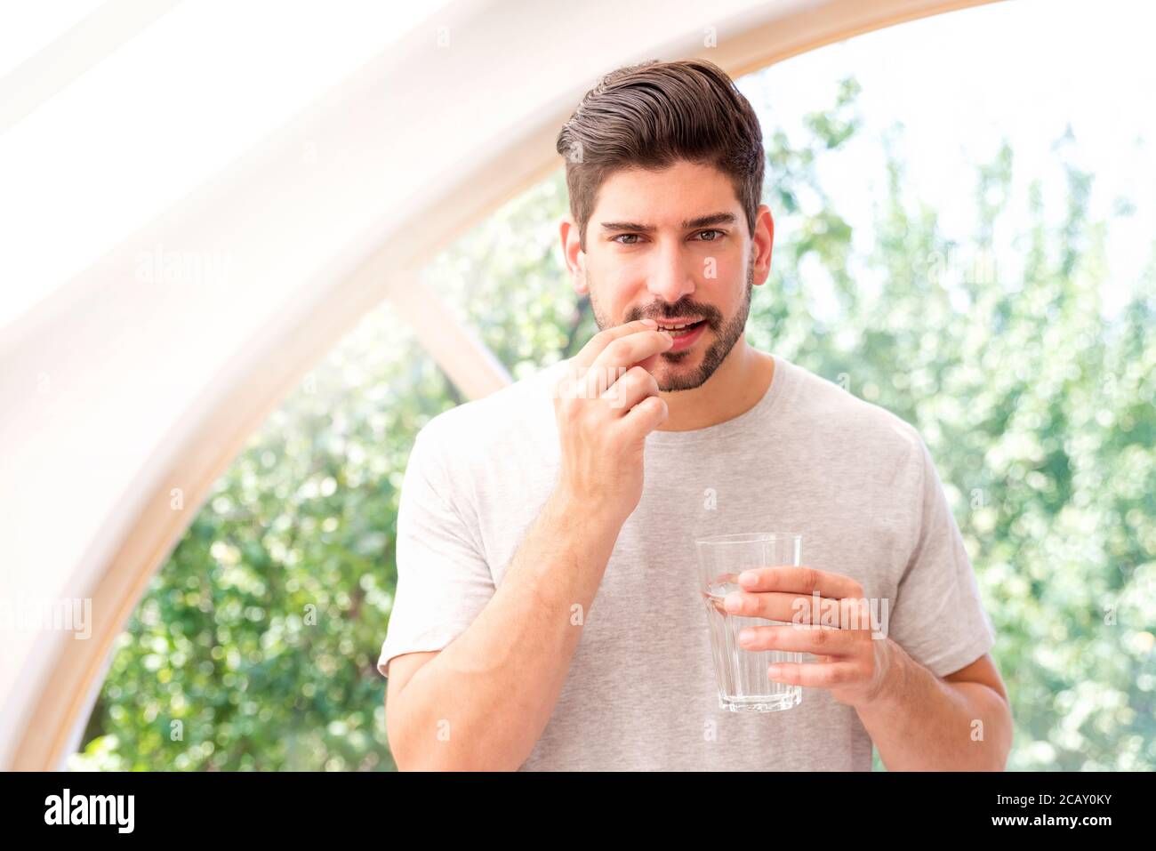 Beau homme tenant un verre d'eau dans sa main tout en prenant la pilule. Banque D'Images