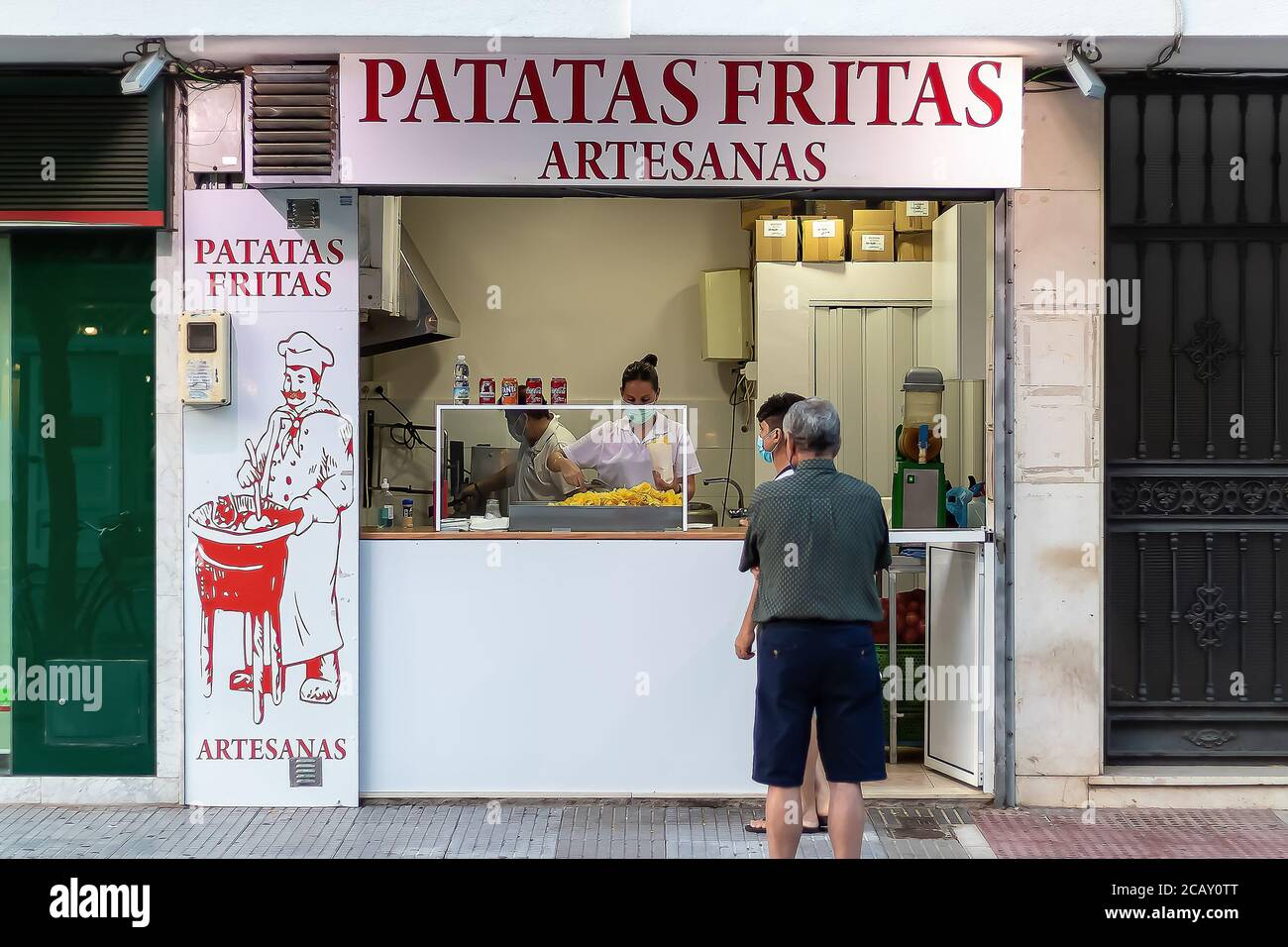 Punta Umbria, Huelva, Espagne - 7 août 2020 : le vendeur dans un local vend des chips de pommes de terre. Les pommes de terre frites sont des aliments typiques de la rue. Elle porte du protec Banque D'Images