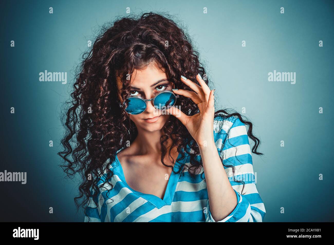 Headshot en colère graves bitchy curly femme wife holding lunettes vers le bas en vous regardant avec scepticisme bleu fond Mur isolé, chemise bleue. Les droits de l'aec Banque D'Images